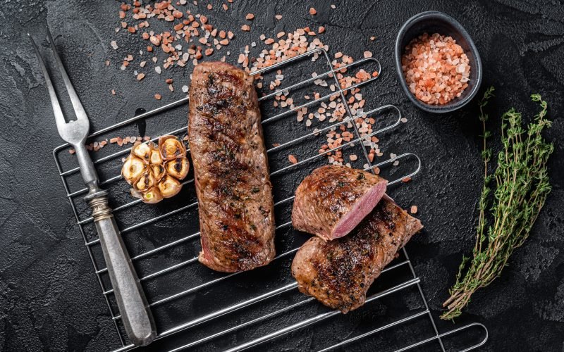 BBQ grilled Lamb tenderloin fillet meat on grill, mutton loin steak. Black background. Top view.