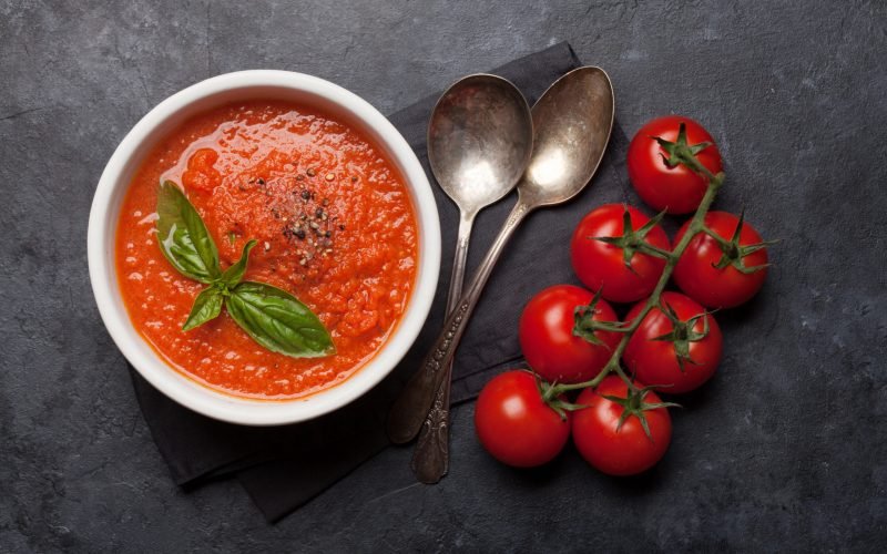 Cold gazpacho soup with ripe tomatoes, cucumber and basil on stone table. Top view flat lay