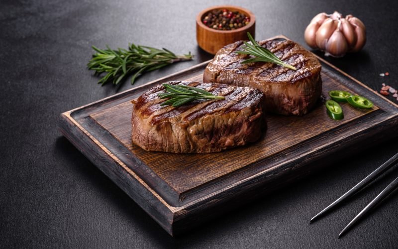 Fresh juicy delicious beef steak on a dark background. Meat dish with spices and herbs