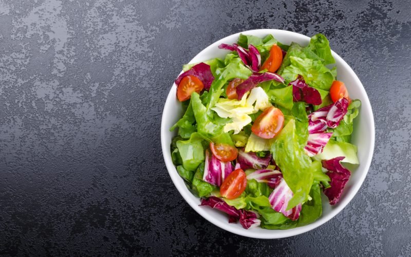 Fresh mixed salad with endive and cherry tomatoes on black plate dining, pouring olive oil