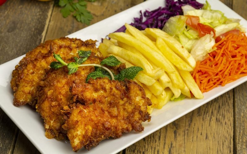 Fried chicken and fries, salads on white plate, wooden table