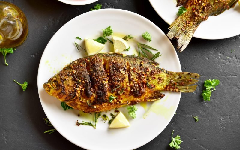 Fried fish on plate over black stone background. Top view, flat lay