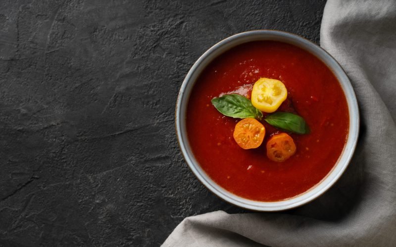 Gazpacho soup with tomato and ingredients on black background, copy space, top view