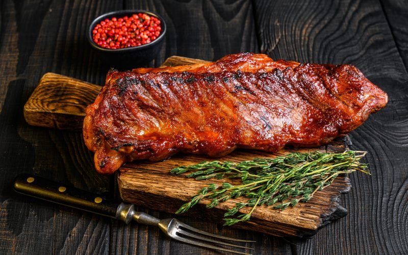 Grilled in bbq sauce veal short spare rib meat on wooden cutting board. Black wooden background. Top view.