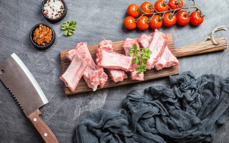 Raw pork ribs with sauce and spices on black background, top view with copy space