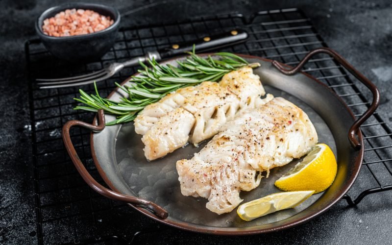 Roast Fillets of codfish, cooked cod fish meat. Black background. Top view.